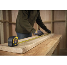 Remeselník meria drevenú dosku zvinovacím metrom Stanley Fatmax, dĺžka 5 metrov.