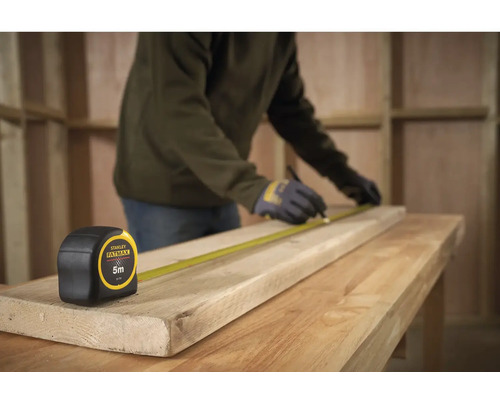 Remeselník meria drevenú dosku zvinovacím metrom Stanley Fatmax, dĺžka 5 metrov.