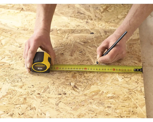 Osoba meria kus dreva pomocou zvinovacieho metra Stanley Fatmax s dĺžkou 5 metrov a označuje ho ceruzkou.