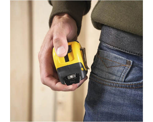 Osoba drží žltý zvinovací meter s klipom na opasok.