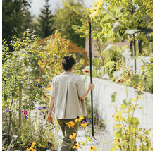 Žena v záhrade s hrabľami a kultivátorom medzi kvetinovými záhonmi