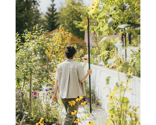Žena v záhrade s hrabľami a kultivátorom medzi kvetinovými záhonmi