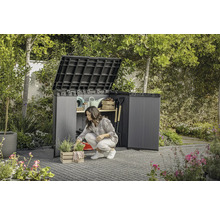 Záhrada so ženou kľačiacou pred otvorenou záhradnou skriňou, v ktorej je uložené záhradné náradie.