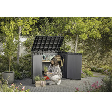 Záhradná scéna s otvorenou skriňou na náradie, do ktorej žena ukladá záhradné náčinie.