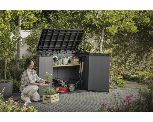 Žena sadí kvety pred otvorenou záhradnou skriňou so záhradným náradím