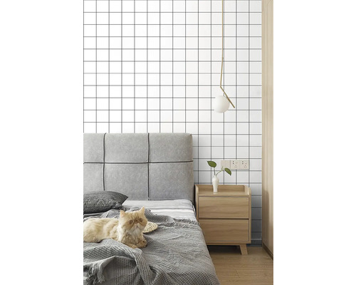 Spálňa s posteľou, nočným stolíkom, lampou a tapetou so štvorcovým vzorom.