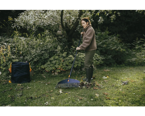 Žena hrabe lístie v záhrade hrabľami na lístie a záhradným vrecom.