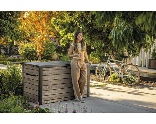 Záhradná scéna so ženou opierajúcou sa o drevený úložný box a držiaci šálku kávy.