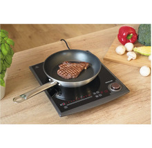 Indukčná varná doska so steaky na panvici a zeleninou na krájacej doske