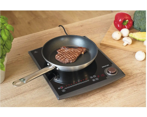 Indukčná varná doska so steaky na panvici a zeleninou na krájacej doske