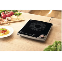 Indukčná varná doska na drevenom stole s prísadami a tanierom špagiet.