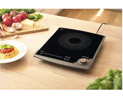 Indukčná varná doska na drevenom stole s prísadami a tanierom špagiet.