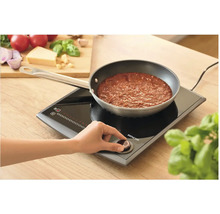 Indukčná varná doska s hrncom a osobou ovládajúcou regulátor teploty