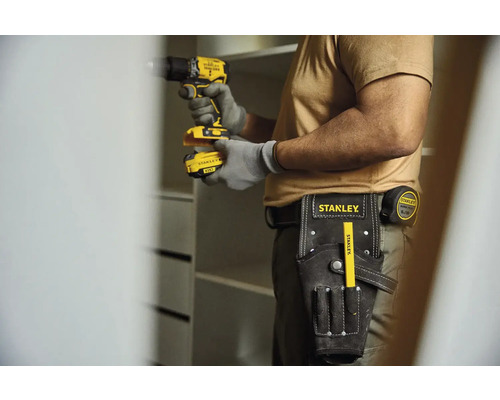 Remeselník s akumulátorovým skrutkovačom, opaskom na náradie a skladacím metrom stavia skriňu