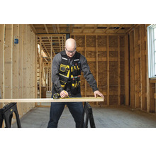 Remeselník meria drevenú dosku pomocou zvinovacieho metra na dvoch kozách v hrubej stavbe.