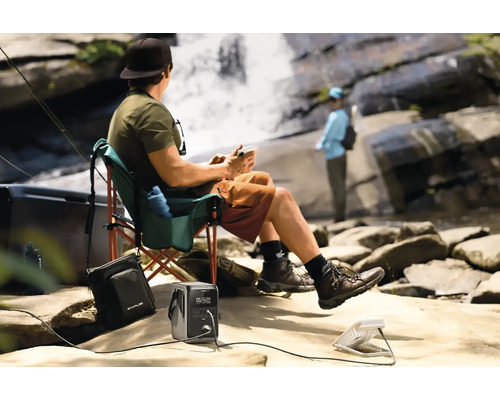 Osoba relaxuje s prenosným zdrojom energie a ventilátorom pri vodopáde