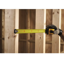 Ruka v rukavici meria drevený rám žltým zvinovacím metrom.