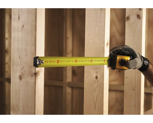 Ruka v rukavici meria drevený rám žltým zvinovacím metrom.