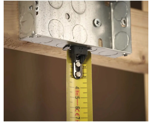 Kovová inštalačná krabica so žltým zvinovacím metrom na meranie na drevenej konštrukcii