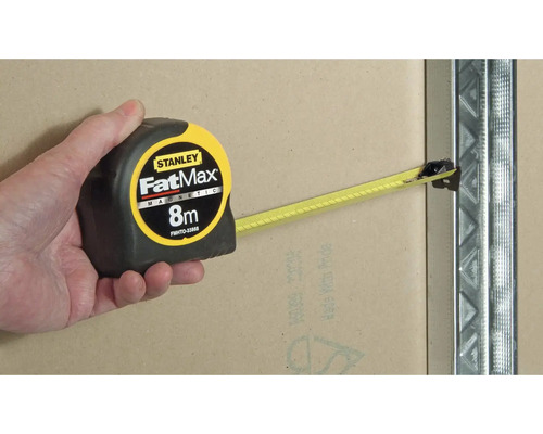 Ruka drží magnetický zvinovací meter Stanley FatMax 8 metrov na kovovom stĺpiku.