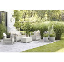 Záhradný nábytok so sedačkou, kreslom a stolom na terase so zeleným trávnikom a rastlinami.