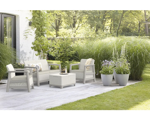 Záhradný nábytok so sedačkou, kreslom a stolom na terase so zeleným trávnikom a rastlinami.