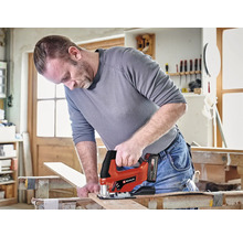 Muž reže drevenú dosku akumulátorovou priamočiarou pílou Einhell v dielni.