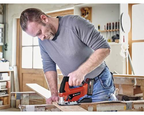 Muž reže drevenú dosku akumulátorovou priamočiarou pílou Einhell v dielni.