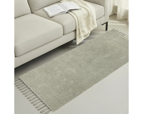 Sivý behúň so strapcami vedľa pohovky s knihou