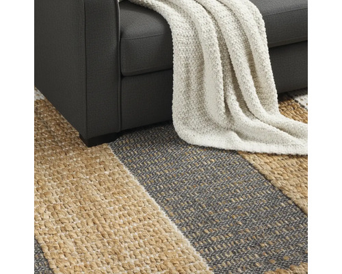 Detailný pohľad na pruhovaný koberec pod pohovkou s dekou.