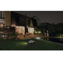 Robotická kosačka na trávu pri nočnej práci v záhrade s domom a bazénom.