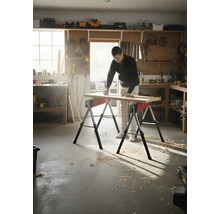 Muž brúsi drevenú dosku na dvoch kozách v dielni.