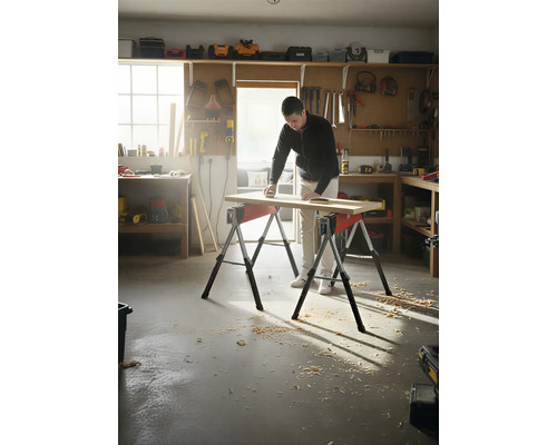 Muž brúsi drevenú dosku na dvoch kozách v dielni.