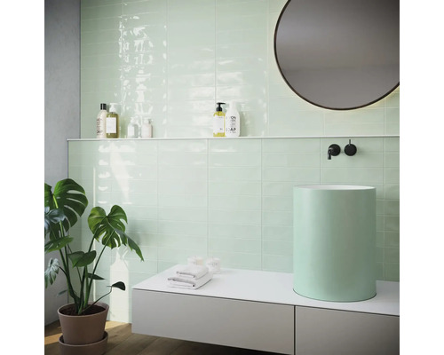 Moderná kúpeľňa s mätovo zelenými obkladmi, umývadlom na dosku a okrúhlym zrkadlom