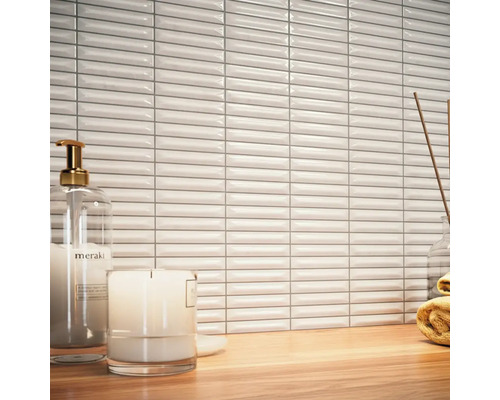 Scéna s bielymi, podlhovastými obkladačkami, dávkovačom mydla, sviečkou a uterákom na drevenom stole