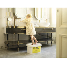 Kúpeľňa s umývadlovou skrinkou, zrkadlami a malým dieťaťom stojacim na vedre, aby dosiahlo na umývadlo.