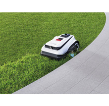 Robotická kosačka na trávniku vedľa dláždenej cesty