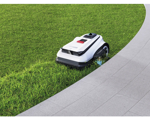 Robotická kosačka na trávniku vedľa dláždenej cesty