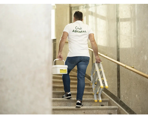 Muž nesie vedro s farbou a rebrík po schodoch