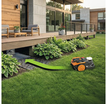 Robotická kosačka na trávu vchádza pod drevenú terasu so zelenou smerovou šípkou.