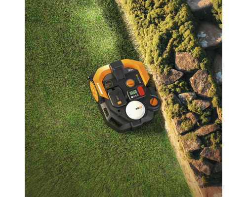 Pohľad zhora na robotickú kosačku na trávniku vedľa kamennej steny