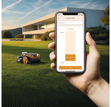 Scéna s robotickou kosačkou a smartfónom so zobrazením nastavenia výšky kosenia na trávniku pred domom.