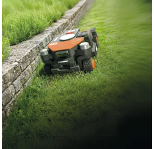 Robotická kosačka LandRoid na trávniku vedľa kamennej steny