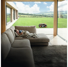 Scéna s chlapcom ležiacim na pohovke, zatiaľ čo robotická kosačka pracuje v záhrade