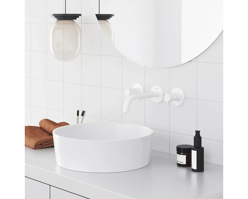 Svetlá kúpeľňa s umývadlom na dosku, batériou, zrkadlom, uterákmi a ošetrujúcimi produktmi