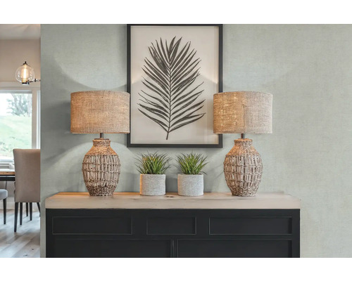 Dekoratívny interiér s dvoma stolnými lampami, umelými rastlinami a zarámovanou potlačou listov na komode.