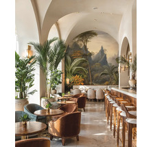 Svetlý bar s klenutými stropmi, tropickou nástennou maľbou, dreveným nábytkom, zamatovými kreslami a veľkými palmami v kvetináčoch.