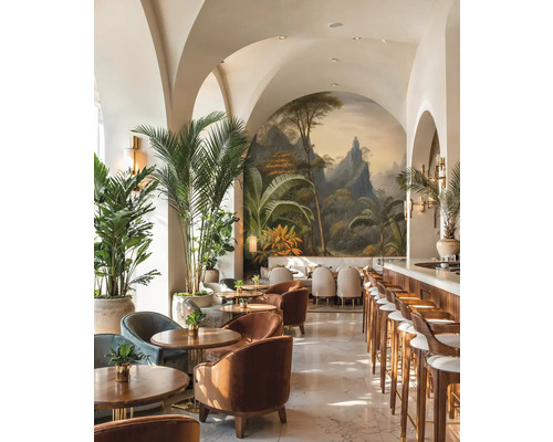 Svetlý bar s klenutými stropmi, tropickou nástennou maľbou, dreveným nábytkom, zamatovými kreslami a veľkými palmami v kvetináčoch.