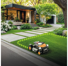 Robotická kosačka na trávniku pred domom s dláždenou cestou