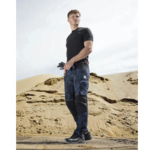 Muž v pracovnom odeve s pracovnými nohavicami, tričkom a bezpečnostnou obuvou pred piesočným kopcom